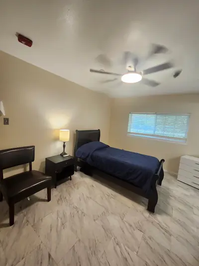 Private bedroom with a bed, blue bedding, nightstand lamp, and ceiling fan